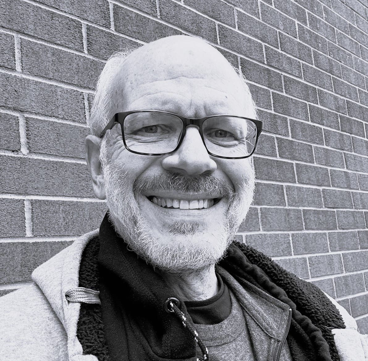 Smiling person standing against a brick wall.