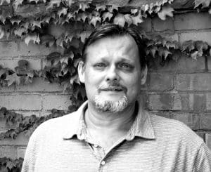 Man in front of brick wall covered with ivy.