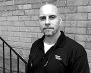 Man standing in front of a brick wall with a serious expression.
