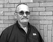 Man in a collared shirt stands against a brick wall.