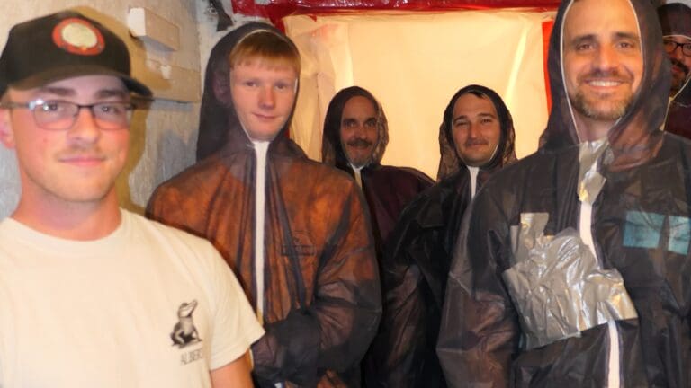 Group of people in protective suits smiling in a dimly lit area.
