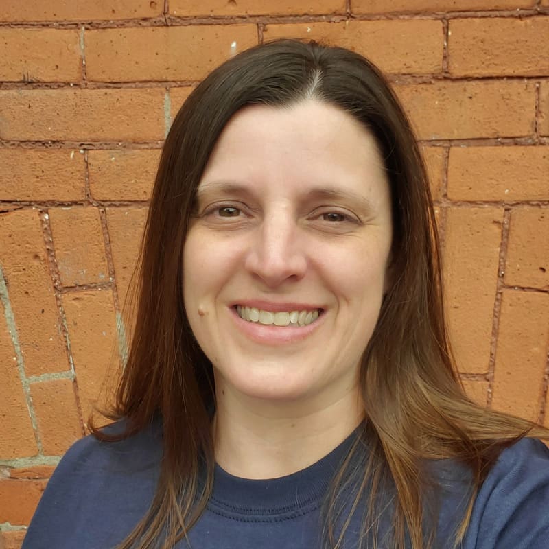 A person smiling in front of a brick wall.