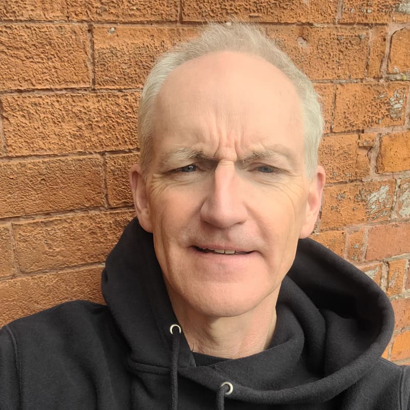 Person in black hoodie standing by a brick wall.