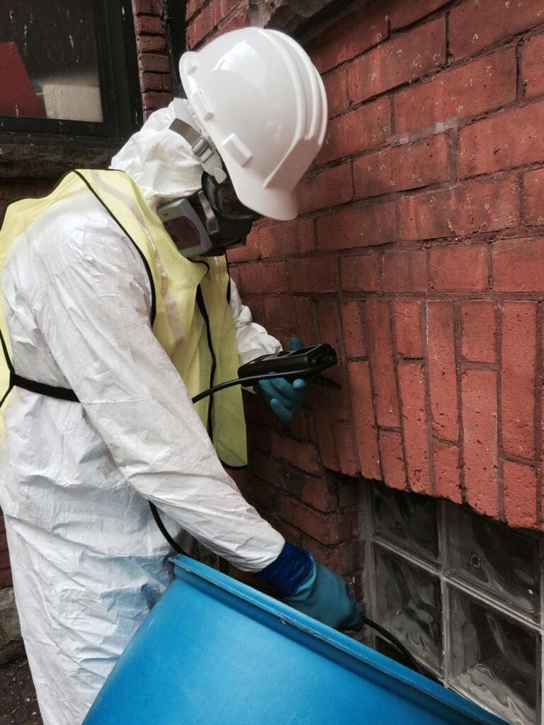 Person in protective gear inspecting brick wall with tools.
