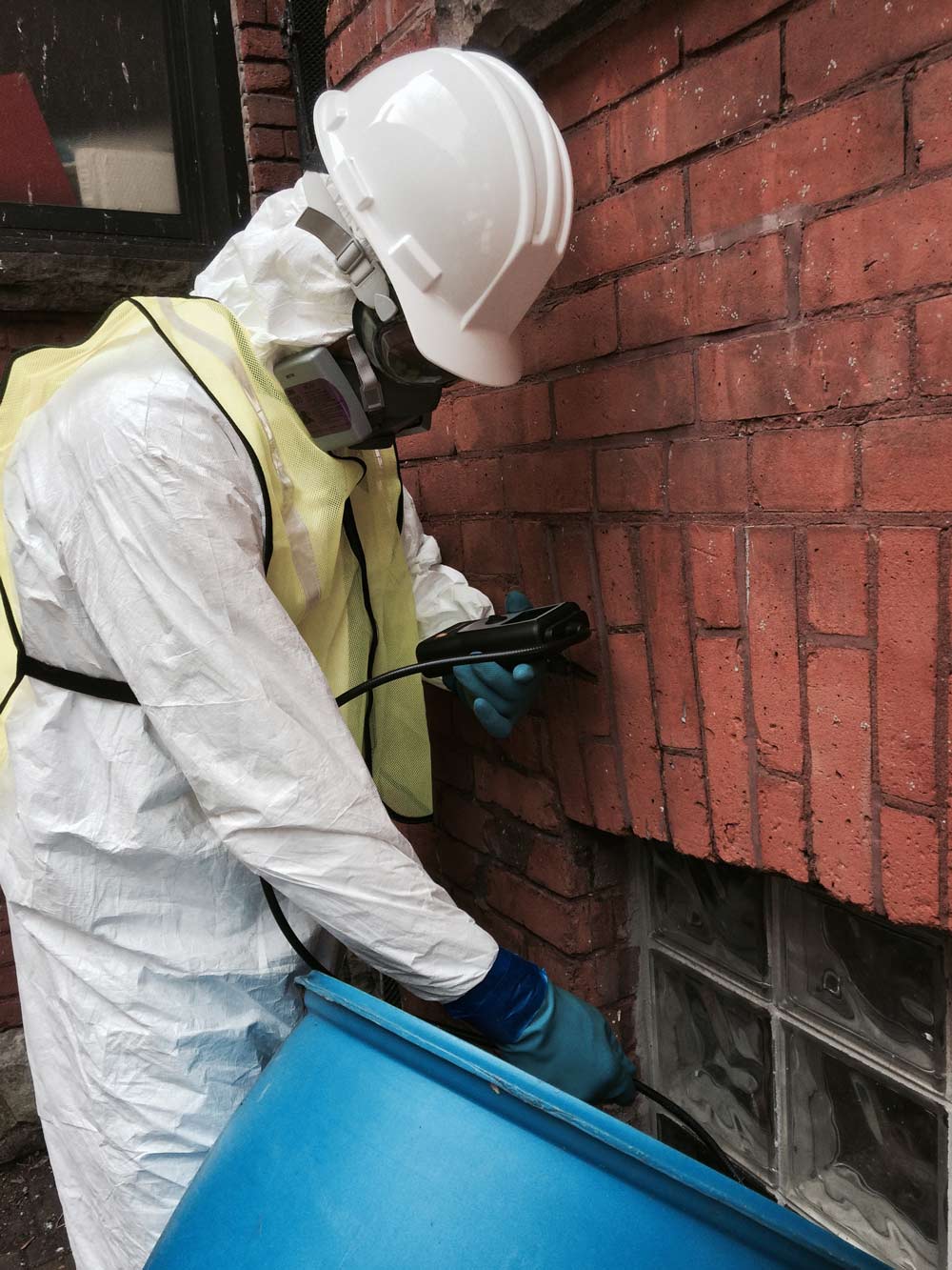 Person in protective gear inspecting brick wall with tools.