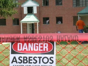 Danger sign warning of asbestos near a building under inspection.
