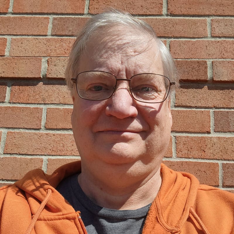 Man in orange hoodie standing in front of a brick wall.