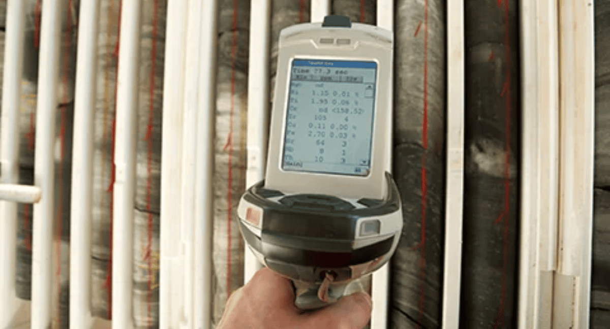 Handheld device displaying scientific data with core samples in background.