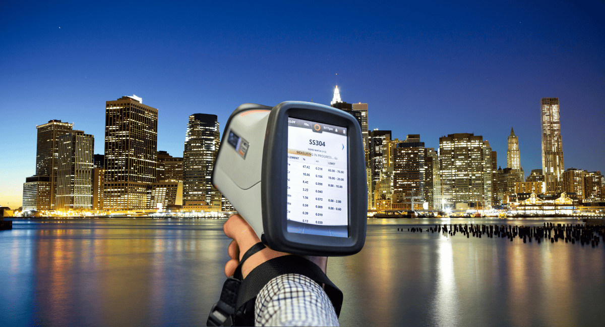 Handheld spectrometer analyzing material with city skyline in background.
