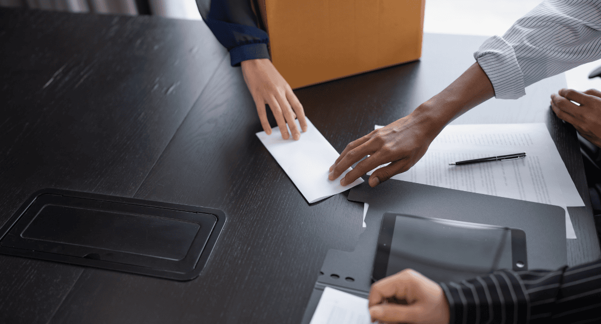 Hands exchanging an envelope over a desk with documents.