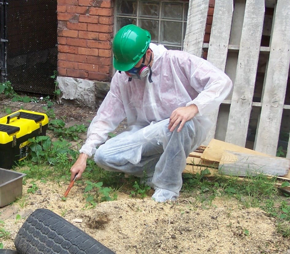 Person in protective gear inspecting ground with toolkit nearby.