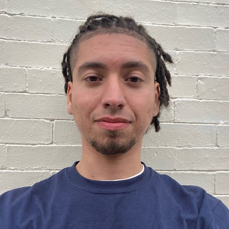 Person with short dreadlocks against a brick wall.