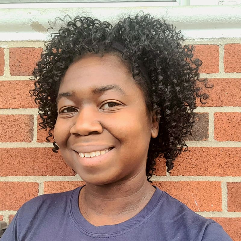 Smiling person standing in front of a brick wall.