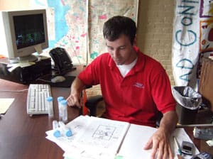 Man in red shirt working at desk with papers and test tubes.