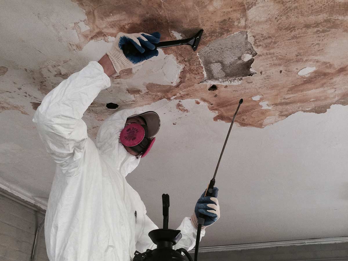 Person removing mold from the ceiling wearing protective gear.