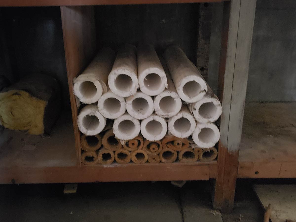 Stacked PVC pipes on a wooden shelf in a storage area.