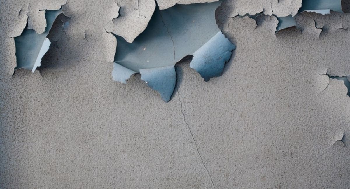 Cracked, peeling gray wall revealing blue paint beneath.