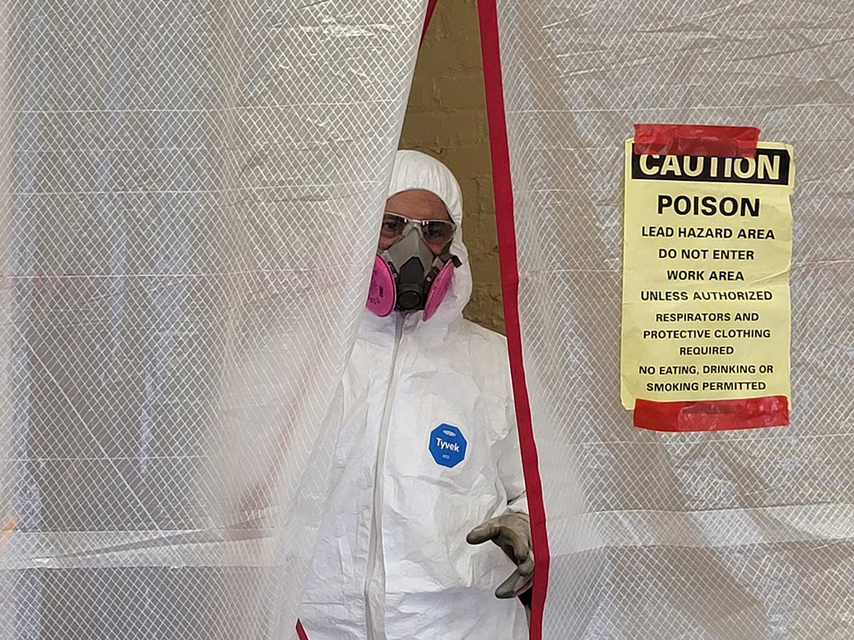 Worker in protective suit near lead hazard warning sign.